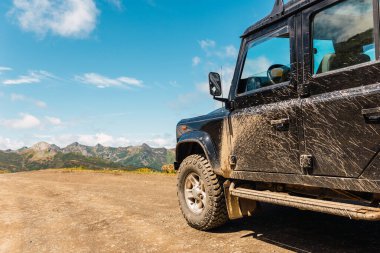 Dağ yolunda çamur ve toz lekesi olan siyah 4x4 off-road arabası
