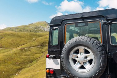 Arkasında yedek siyah 4x4 off-road arabasıyla dağda park halinde.