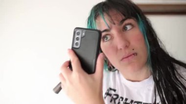 Alternatif piercingli kız makyaj rutininde başarısız oluyor, akıllı telefonuna bakarken yüzünün her tarafına allık sürüyor.