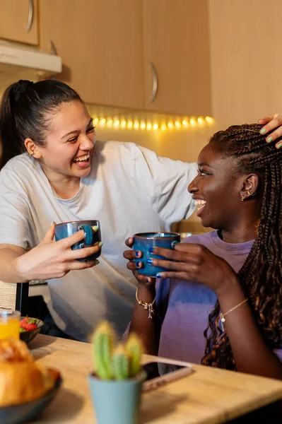 İki kadın gülüyor ve kahvaltının tadını çıkarıyor. Mutfaklarında, kahve içip sohbet ediyorlar.