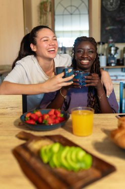 Mutlu kız arkadaşlar sağlıklı bir kahvaltıyı çilek, avokado ve meyve suyuyla paylaşıyor. Aşkı ve birlikteliği simgeliyor.
