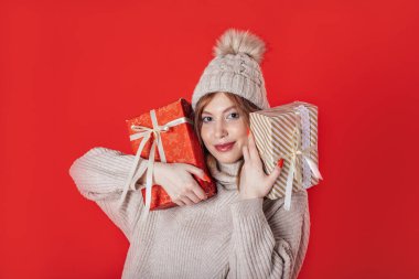 Güzel, genç bir kış kızı elinde kırmızı arka planda bir Noel hediyesi tutuyor.