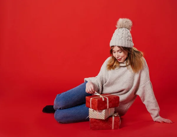 Dreaming zima dziewczyna siedzi gospodarstwa Boże Narodzenie obecny na czerwonym tle — Zdjęcie stockowe