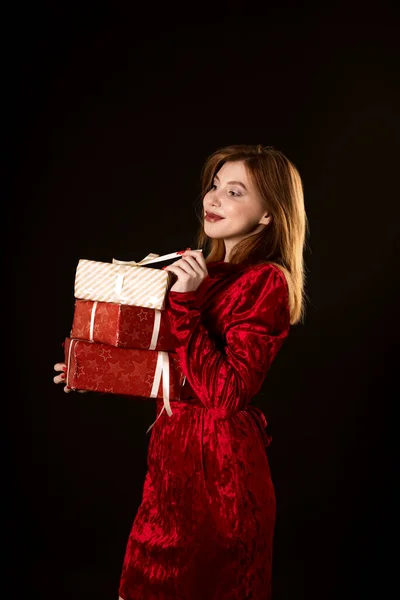 Dziewczyna w czerwonej sukience na czarnym tle trzyma prezent w dłoni. — Zdjęcie stockowe