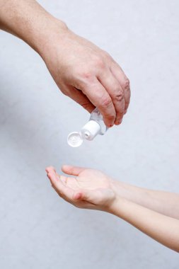 Bir çocuğun elini dezenfektan alkol jeliyle işleyen bir yetişkinin resmi.