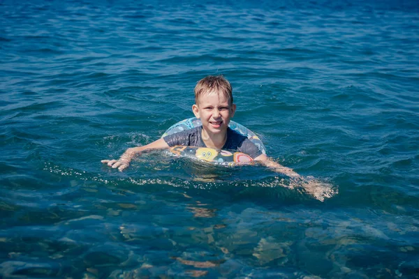 Blondýnka chlapec plavání v moři na nafukovací kroužek — Stock fotografie