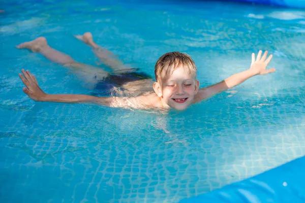 穿着蓝色泳裤的金发男孩在一个充气游泳池里游泳 — 图库照片
