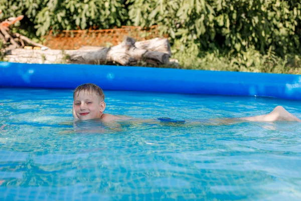 Blonde boy in blue swimming trunks swims in an inflatable pool — Stock Photo, Image