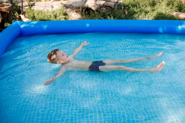 Ξανθό αγόρι με μπλε μαγιό κολυμπάει σε μια φουσκωτή πισίνα — Φωτογραφία Αρχείου