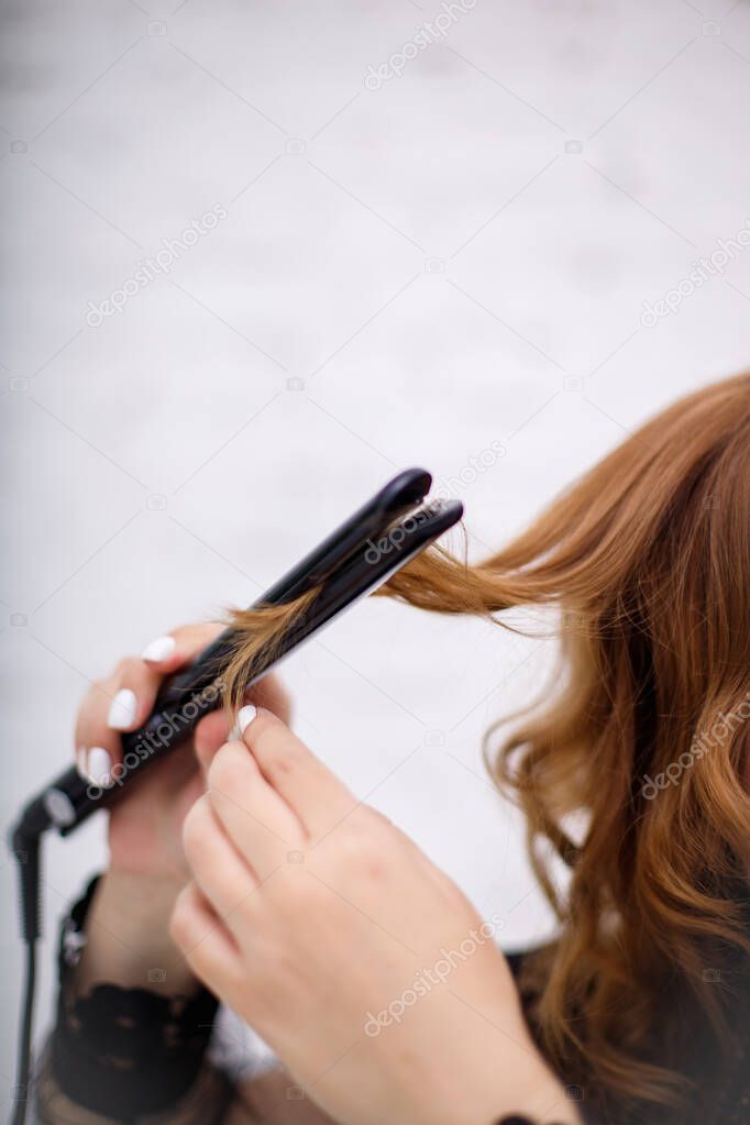 A girl with red hair straightens them using electric irons.