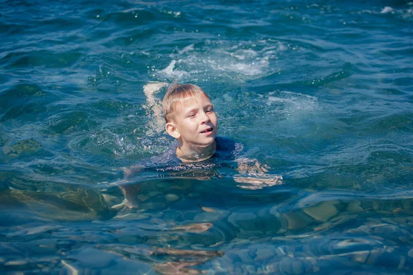 Blonďatý chlapec plave v létě v moři — Stock fotografie