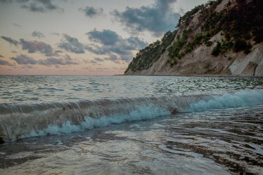 Seascape against the backdrop of a sunset sky with clouds and a huge cliff.