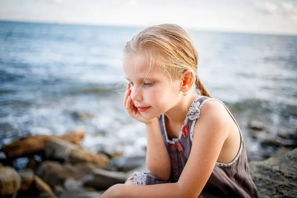 Ένα ξανθό κορίτσι με ένα φόρεμα κάθεται σε μια πέτρα στην ακτή.. — Φωτογραφία Αρχείου