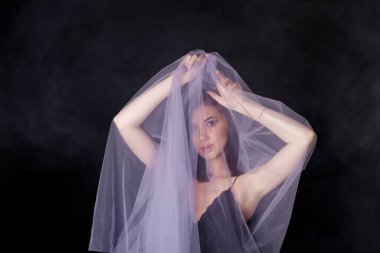 Siyah elbiseli esmer kız leylak peçeye sarılmış elleri kapalı duruyor.