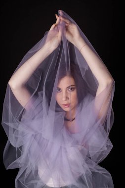 Siyah elbiseli esmer kız leylak peçeye sarılmış elleri kapalı duruyor.