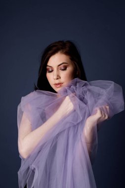 Siyah elbiseli esmer kız, leylak peçeye sarılmış.
