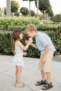 Çocuklar bir şehir parkında birbirlerine dondurma yedirirler. Tatlı.
