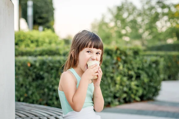 Chica en un vestido ligero come helado de paleta en un parque de la ciudad. Los niños descansan en el verano. — Foto de Stock