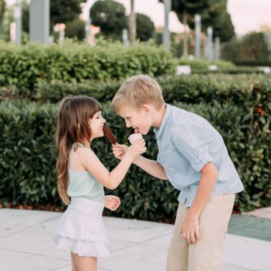 Çocuklar bir şehir parkında birbirlerine dondurma yedirirler. Tatlı.