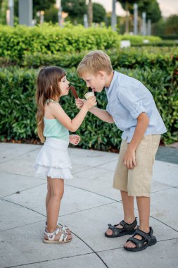 Çocuklar bir şehir parkında birbirlerine dondurma yedirirler. Tatlı.