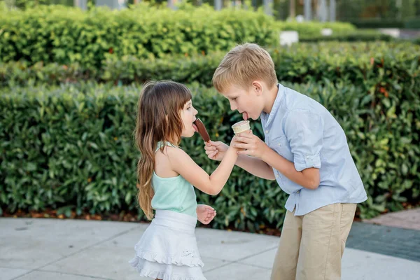 As crianças alimentam um a outro sorvete em um parque da cidade. Sobremesa — Fotografia de Stock