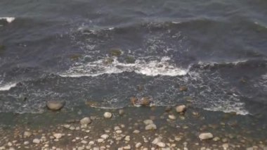 Deniz dalgaları kıyıda yuvarlanıyor ve kayalarda kırılıyor.