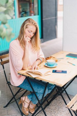 Kafeterya terasında kitap okuyan yakışıklı sarışın kadın..