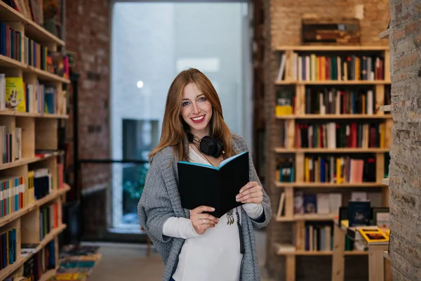 Νεαρή Ξανθιά Γυναίκα Ένα Βιβλίο Ένα Βιβλιοπωλείο Χαμογελώντας Και Κοιτάζοντας — Φωτογραφία Αρχείου
