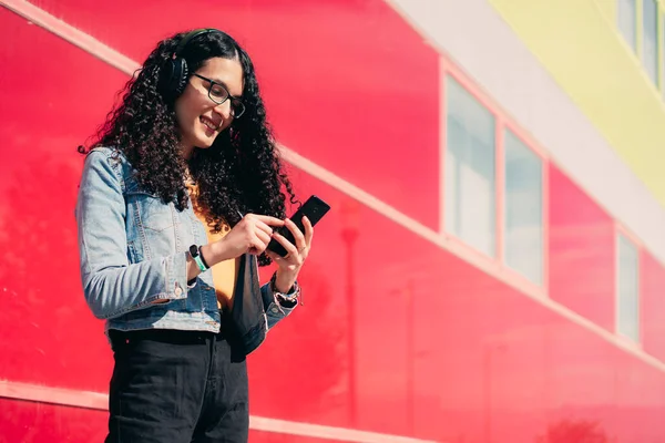 LGTB transgender girl with curly hair on a red and green wall sending a message with her cell phone