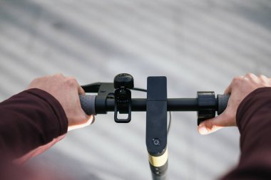 Elektrikli scooter 'ın gidonunu tutan birinin ellerine yakın çekim.