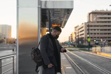 Maskeli işadamı, saatine bakarken treni bekliyor..