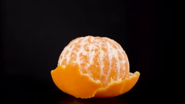 Mandarina pelada girando lentamente con cáscara. Tangerina aislada en negro — Vídeos de Stock