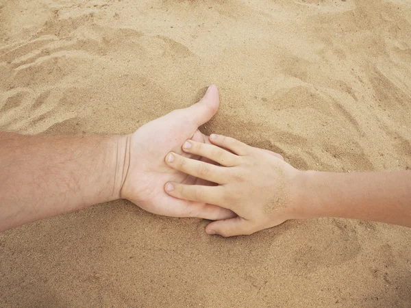 Father and son hands on sand. Close up