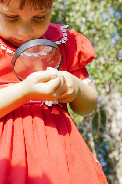 Девушка смотрит через увеличительное стекло на траву на открытом воздухе
