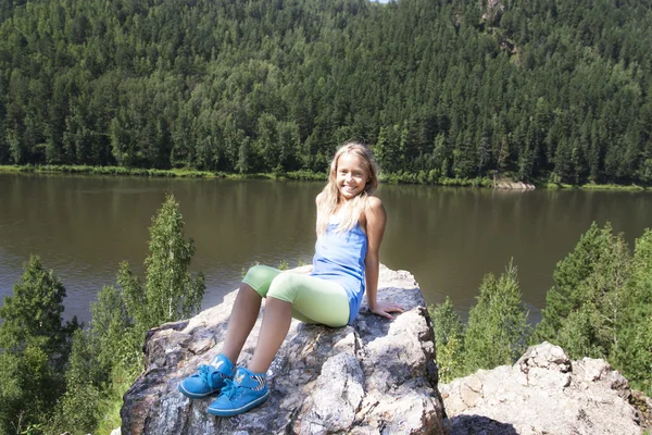 Kayanın üzerinde oturan ve nehir manzarası keyfi kız — Stok fotoğraf