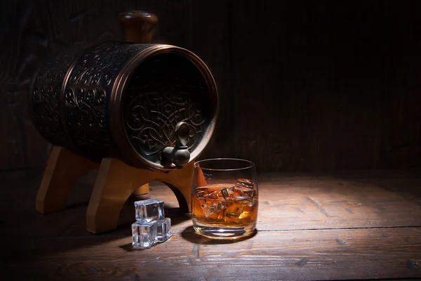 Glass of whiskey  with ice  beside a barrel on wooden backgroun — Stockfoto