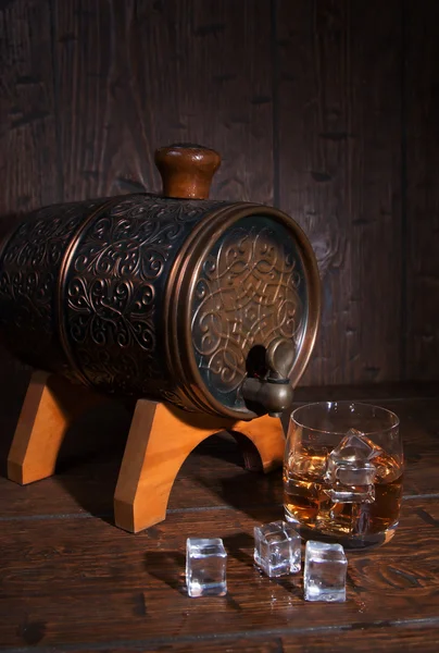 Glass of whiskey  with ice  beside a barrel on wooden backgroun — Stockfoto