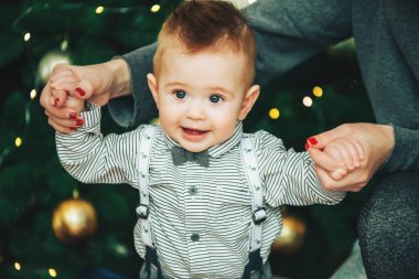 Küçük çocuk ilk adımlarını atar annesinin elini tutarak Noel ağacının arka planında
