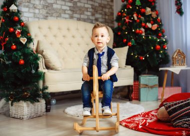 Mutlu yıllar için Noel ağacının önünde ata binen sevimli çocuk.