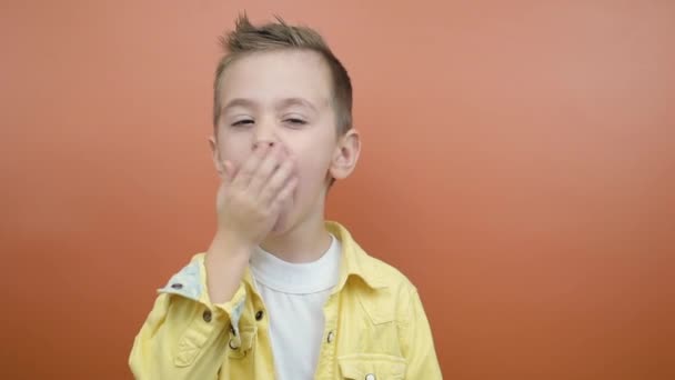 Ein gelangweiltes, schläfriges Kind gähnt isoliert vor orangefarbenem Hintergrund — Stockvideo