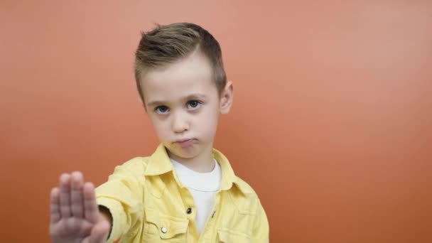 Serious young kid waving finger no hand sign look at camera isolated orange background — Stock Video