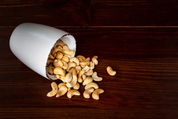 Scattered cashew in a bowl against dark rustic wooden background — Stock Photo, Image