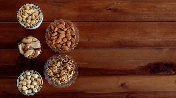 Mixed nuts in different bowls on wooden table — Stock Photo, Image