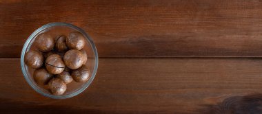 Pankart, koyu ahşap masadaki kasede soyulmamış macadamia ile. Üst görünüm, metin için boşluk