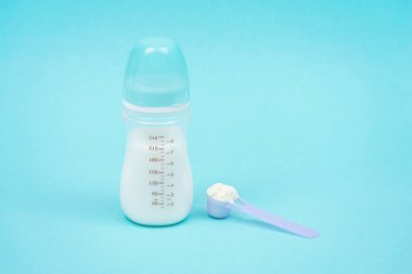 Beslenmek için çocukların kuru karışımı, ölçüm kaşığı, emzik şişesi ve mavi arka plan. Yapay beslenme kavramı