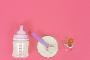 Top view of baby milk powder, baby bottle and dummy on a pink background. flat lay
