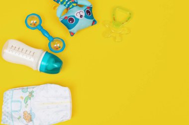 Bir şişe süt formülü diş çıkarma, bebek bezi ve sarı arka planda oyuncaklar. Düz yat, boşluğu kopyala