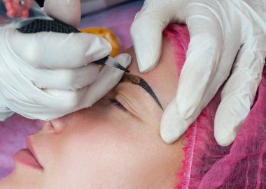 Beyaz eldivenli güzellik uzmanı kalıcı makyaj düzeltme kaşları şekillendiriyor.