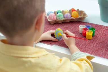 Paskalya yumurtalarını boyayan yaratıcı beyaz çocuk. Anaokulu öğrencisi çocuk paskalya yumurtalarını farklı renklerde dekore edip boyuyor. Paskalya bayramı için hazırlık. Görüntüyü kapat