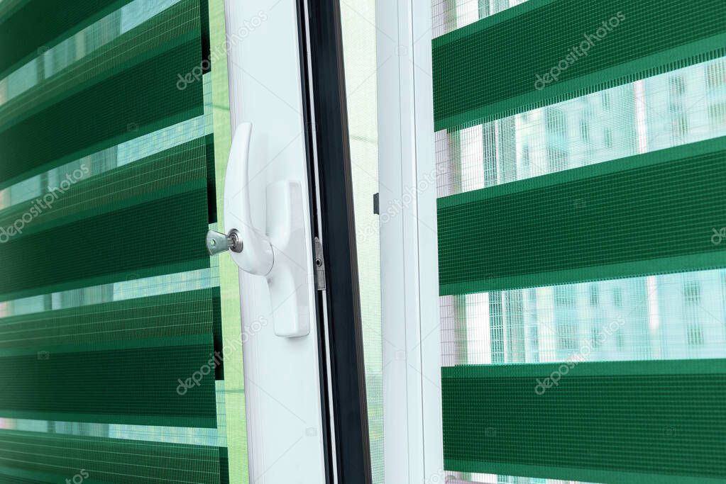 Metal plastic windows with blinds, close up view on handle with a lock. The concept of protecting a child from falling out of windows. Child safety at home concept